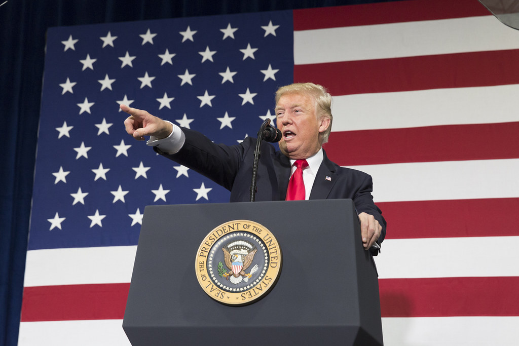 Donald Trump pitää puhujanpöntössä puhetta ja osoittaa eteen vasemmalla kädellään, taustalla Yhdysvaltojen lippu.